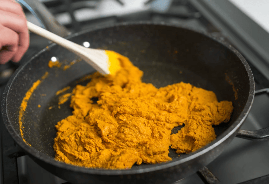 Thick golden-yellow Golden Paste being stirred in a black frying pan on a stovetop